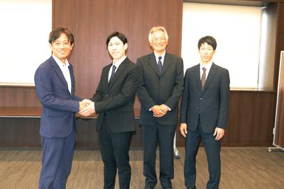 加計理事長(左端)とがっちり握手する田中さん(左から2人目)。その右隣は杉安元顧問、さらに吉澤顧問