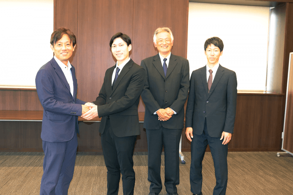 加計理事長(左端)とがっちり握手する田中さん(左から2人目)。その右隣は杉安元顧問、さらに吉澤顧問