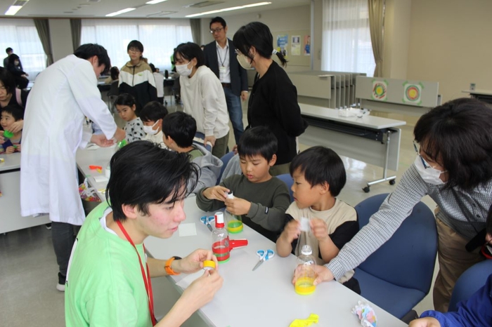 保護者と一緒にペットボトルで「空気銃」を作る子どもたち