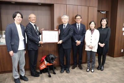 平野学長(右から4人目)に感謝状を手渡す髙野センター長(左から2人目)、二人の間にじっと座っているのが「マックス」