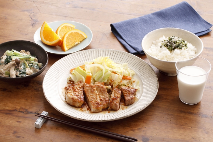 【肉が主役の晩ごはん】厚切り豚のしょうが焼き（★）、小松菜としめじの白あえ、ご飯、牛乳、オレンジ。ボリューム感のあるとんカツ用の豚肉でしっかりたんぱく質をとります。豚肉は糖質をエネルギーに変えるためのビタミンB1が豊富！　添える野菜には、ビタミンB1の吸収を高めるアリシンを含む玉ねぎを加えます。