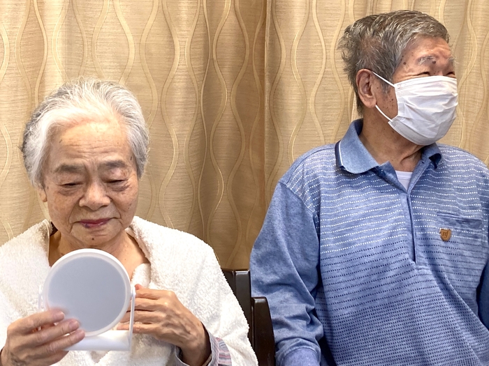 鏡を見る古賀初子さんと嬉しそうなご主人