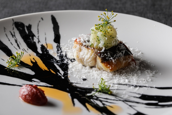 ▲魚料理： 夏に旬を迎える鱸を香ばしく焼き上げました。鱸のエサにもなる烏賊を合わせ食物連鎖をイメージ。チョリソオイルやパルミジャーノ・レジャーノで旨味の相乗効果を、トマトフォンデュの酸味で一皿の全体バランスを加味。