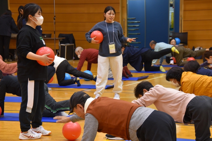 「健康サポート体操」で参加者を見守る学生たち