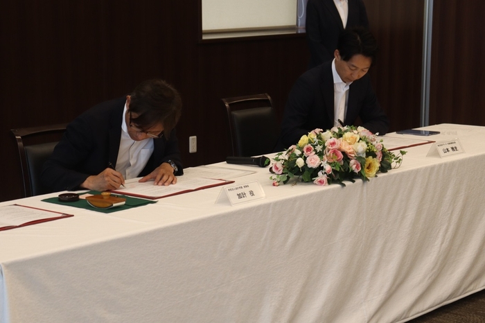 協定書に署名する(左から)加計理事長、山本社長