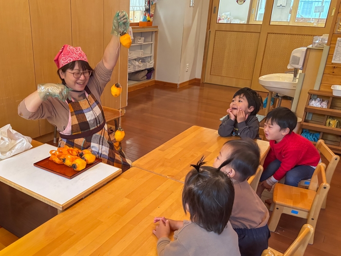 紐で縛った柿を見せる保育者