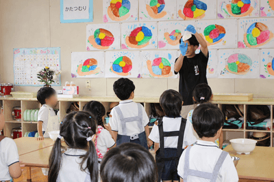 スタッフがうどん作りの工程を実演し、興味深そうに見学する園児たち
