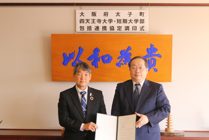 太子町の田中 祐二町長(左)と、須原 祥二学長(右) = 12月15日(木)、背景の「以和為貴」は17条憲法の第1条「和を以て貴しとなす」