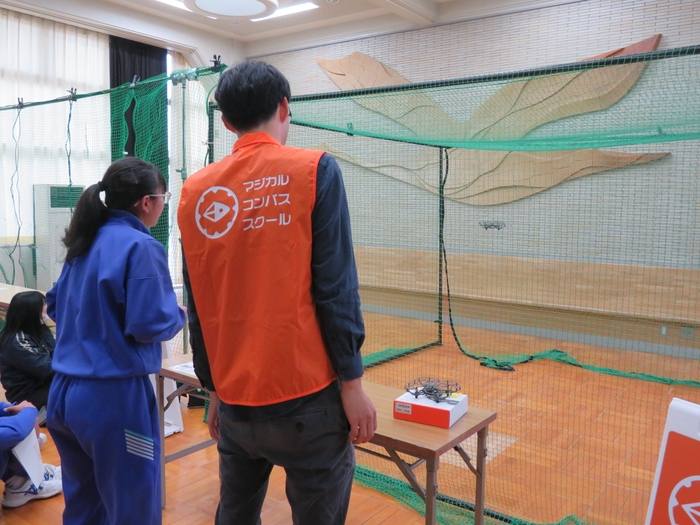 ドローン体験授業の様子（現場で使用するドローンのデモ飛行のほか、生徒代表がトイドローンを実際に操作する操作体験も実施）