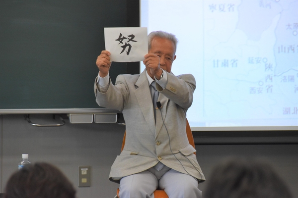 直筆で書かれた「努」を掲げ、夢を持つ大切さを語る橋本さん