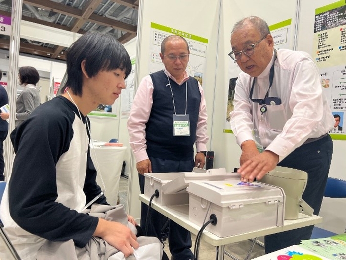 辻教授(右)の説明に聞き入る来場者の大学生。中央は轟代表取締役