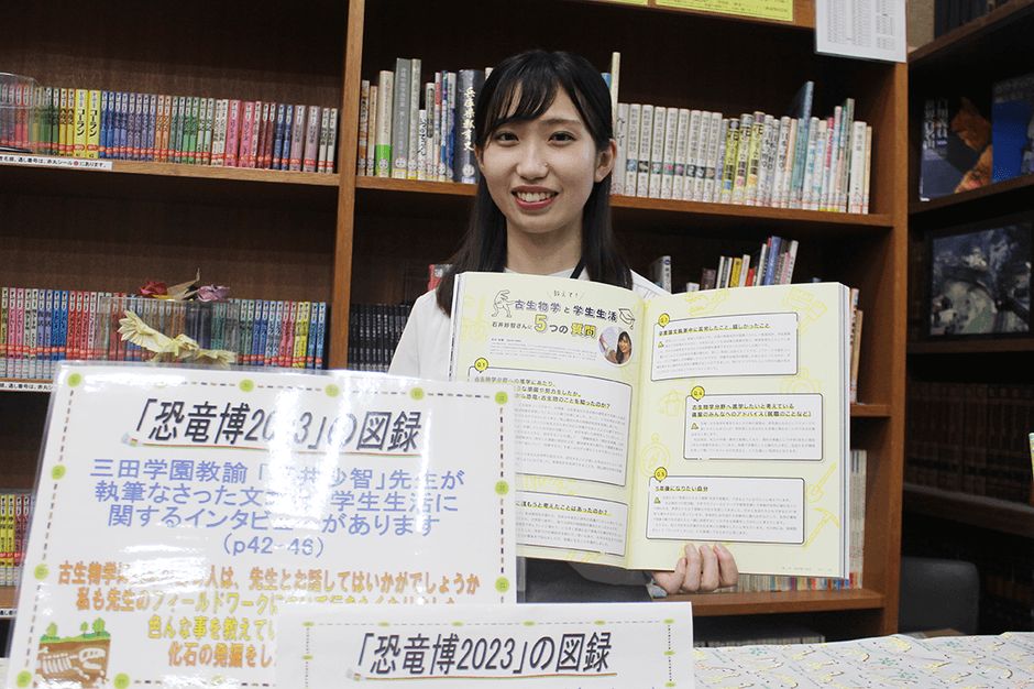 「恐竜博2023」の図録で、自分が紹介されているページを開く石井さん(三田学園中学・高校図書館で)