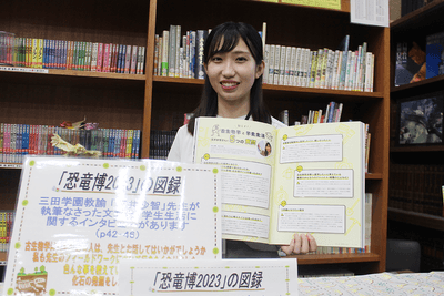 「恐竜博2023」の図録で、自分が紹介されているページを開く石井さん(三田学園中学・高校図書館で)