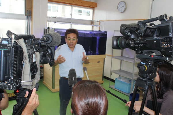 大型水槽前で報道陣の取材に答える山本准教授