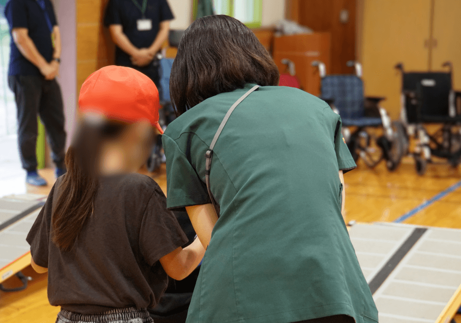 車いすを介助する側も体験。児童が職員と一緒に車いすを押し、移動の難しさを学ぶ
