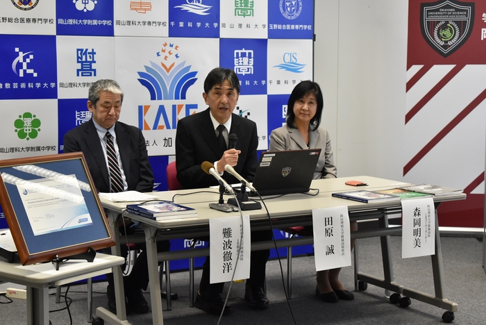 記者会見する田原校長(中央)ら。左側額に認定証