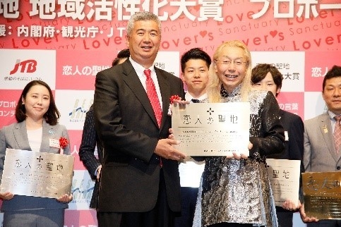 假屋崎省吾さんより銘板を授与されるニジゲンノモリ代表取締役社長 貞松宏茂