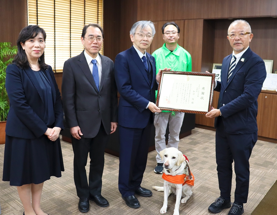 高野センター長(右端)から感謝状を受け取る平野学長(右から3人目)。2人の間で座っているのがPR犬・アクア