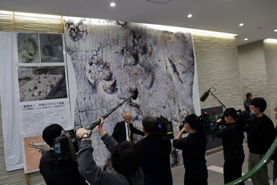 足跡化石の実物大写真の前で解説する石垣名誉館長