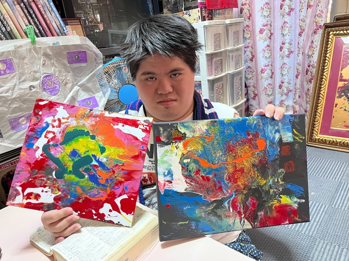 小波津有希さんが制作した2点の鮮やかな抽象画作品を手に持つ様子