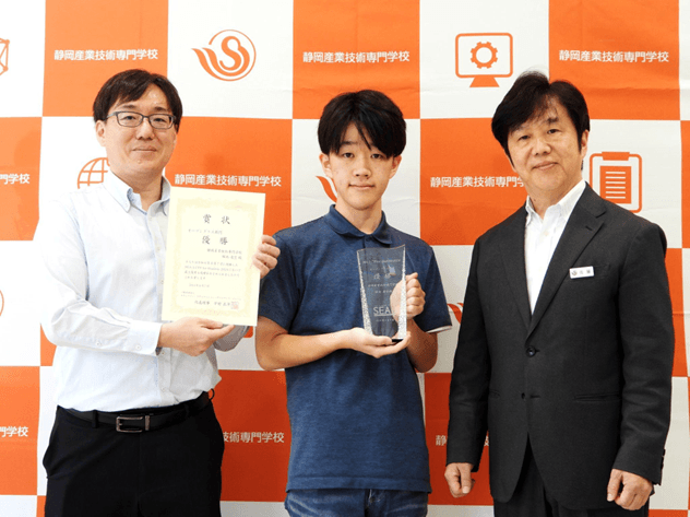 写真は、優勝に輝いた静岡産業技術専門学校(SANGI)みらい情報科2年生、堀池 凌空さんと、塩崎先生と校長の佐藤先生
