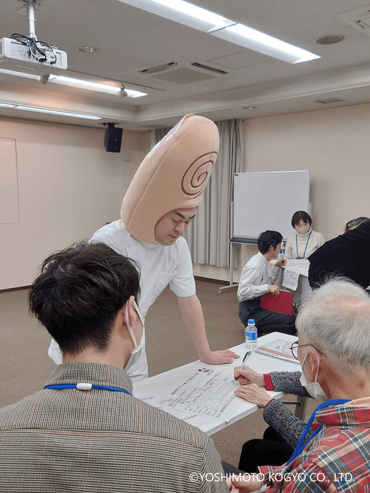 認知症の人および家族と漫才師が漫才プログラムを作成している一コマ <手前:吉本興業芸人 親指ぎゅー太郎さん、後方:(同)吉本興業京都府住みます芸人 木下弱さん>