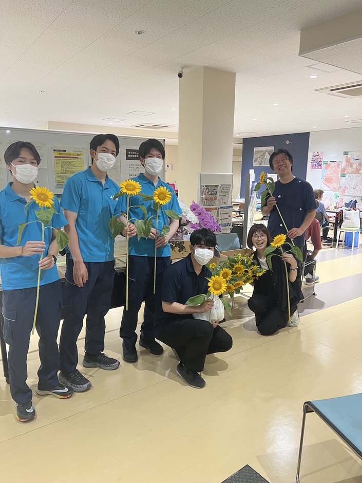受付で福岡市職員の皆様とともに。熊本・五蘭塾 中川洋蘭ご夫妻の胡蝶蘭と、福岡・鶴野さんのひまわりをお届けしました。