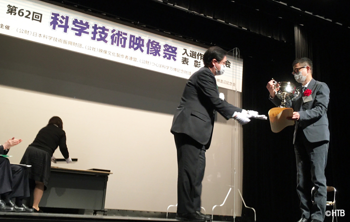 記念のトロフィーを受け取る内閣総理大臣賞を受賞した「たづ鳴きの里」沼田博光ディレクター(写真右)　(C)HTB