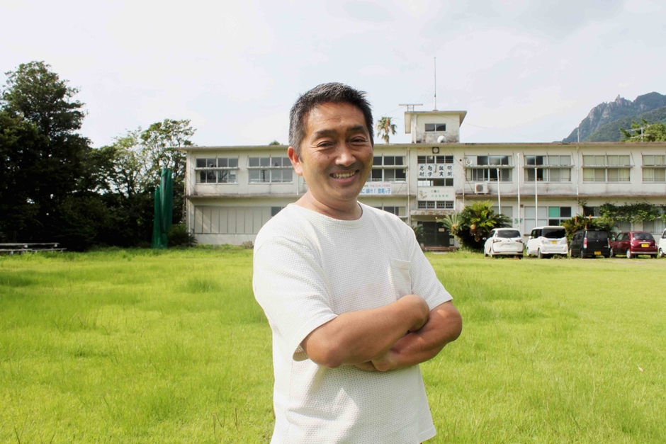 代表 黒木/背景は工場の小学校