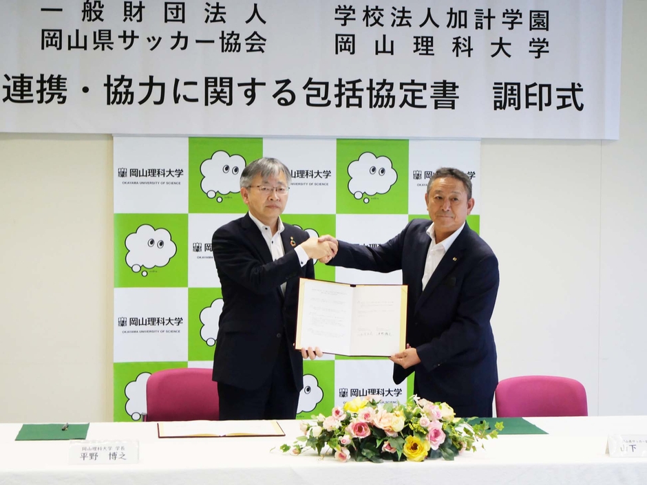 協定書に署名後、がっちり握手する山下会長（右）と平野学長（左）