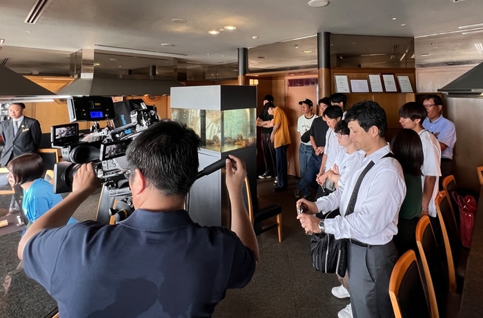 テレビの撮影風景を見学するラボの学生たち=ホテルグランヴィア岡山で