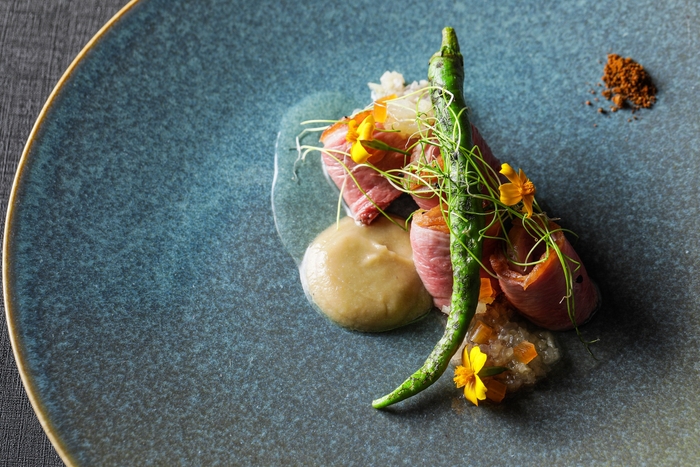 ▲肉料理: 鴨ロース肉の皮面をしっかりと焼き、ジューシーに焼き上げました。焼き茄子のピューレ、甘長唐辛子、生姜と守口漬けのコンフィ、黒七味をあわせ和を感じる優しい味わいに仕上げています。目の前でスモークをかけ、香り高い一品に。