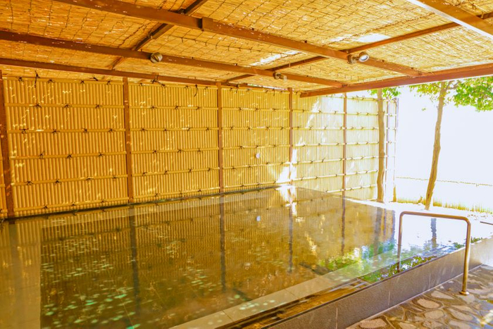 シックな色合いの浴槽とナチュラル素材の囲いが和風モダンの雰囲気を醸す「光彩の湯　露天風呂」。日中は窓から海を眺めることができます。