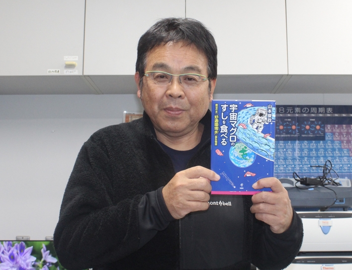 自著の「宇宙マグロのすしを食べるー魔法の水『好適環境水』誕生物語」を手にする山本准教授