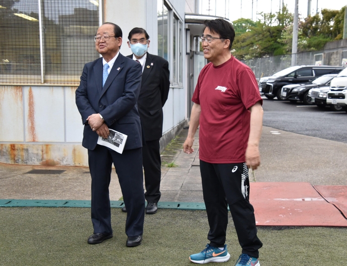 立花理事長、小原学長の横で激励の言葉を述べる大村知事