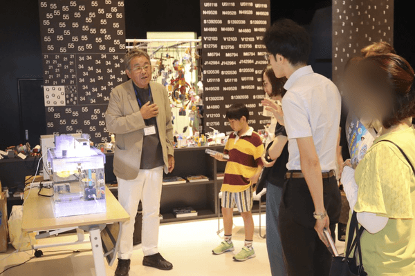 宇宙養殖実験水槽を前に参加者に実験内容を解説する山本准教授（左）