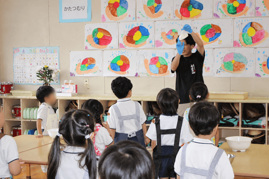 スタッフがうどん作りの工程を実演し、興味深そうに見学する園児たち