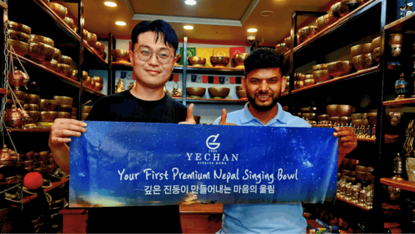 ネパールのシンギングボウル専門店で、YECHAN代表（左）と現地関係者がブランドバナーを掲げる様子