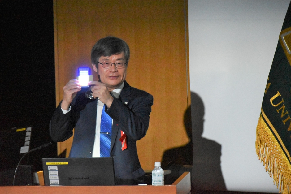 青色LEDで白色光を作る原理を見せながら説明する天野教授